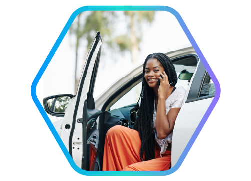 Foto de mulher sentada no banco do motorista do carro parado com a porta aberta e o corpo para fora enquanto olha o celular