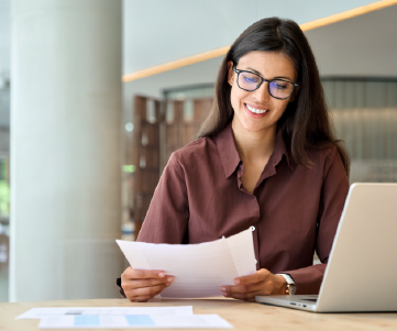 mulher sorrindo com papel na m�o em frente a notebook