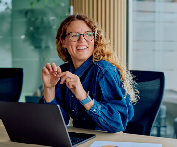 mulher de oculos e cabelos claros sorrindo em frente a notebook